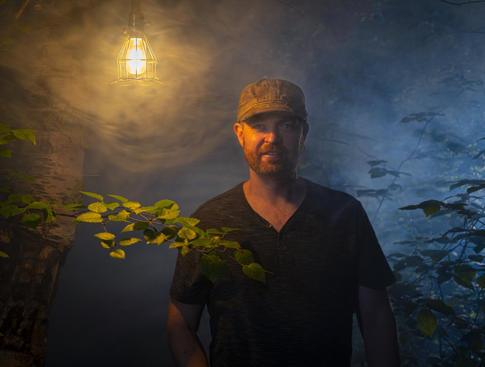 Micheal Lander under a hanging lamp in a misty forest